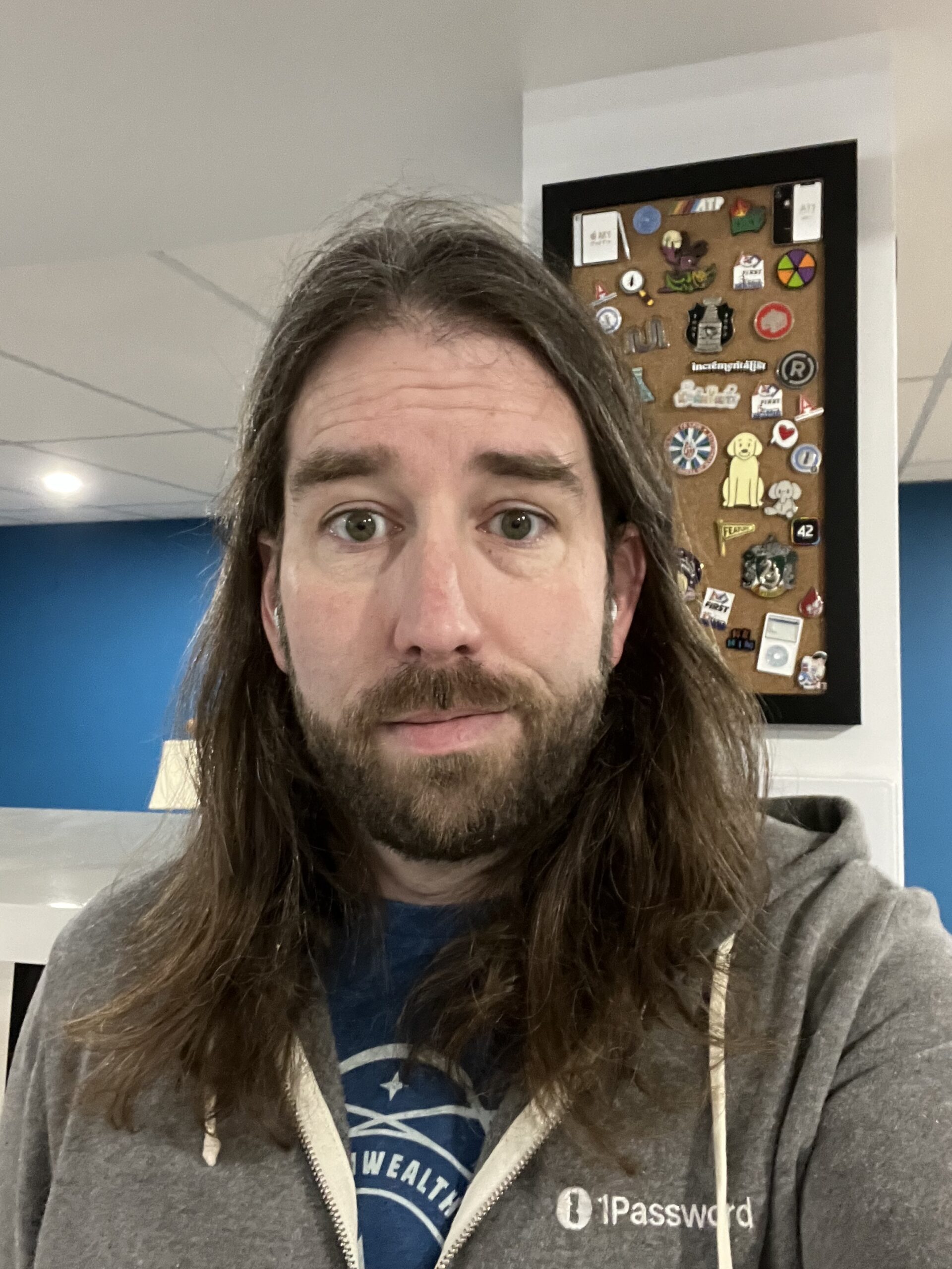 Selfie wearing a grey hoodie standing in front of a pin board with hair long enough that it falls past my shoulders