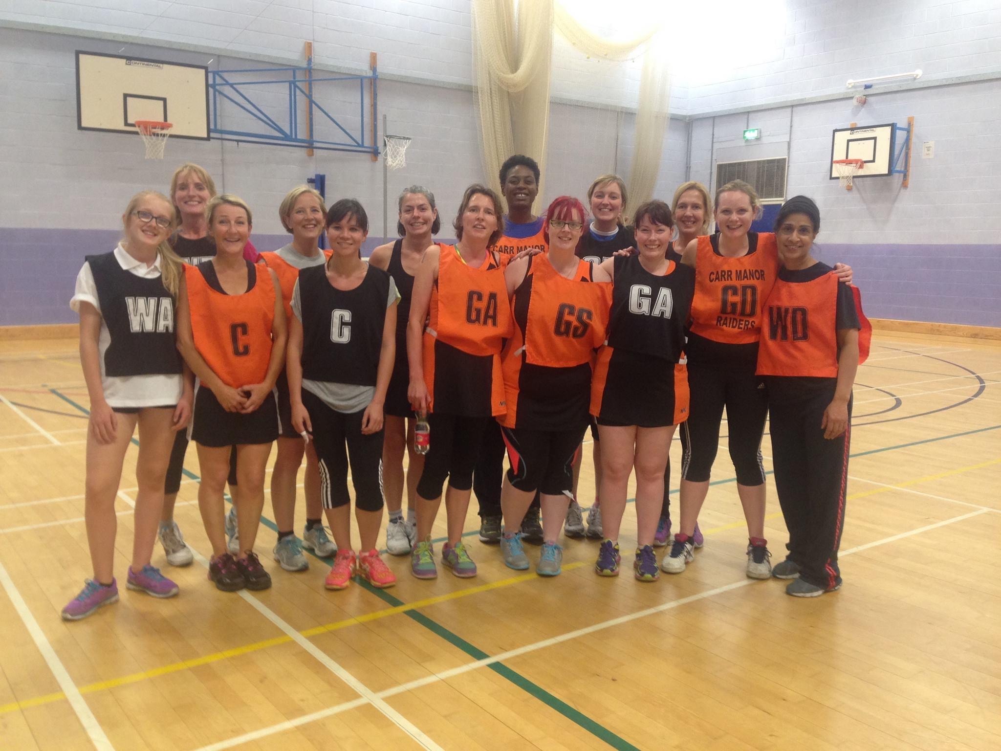 A group of women wearing black or orange netball bibs. 