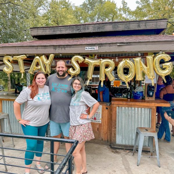 Man and two women in front of balloons spelling "Stay Strong"