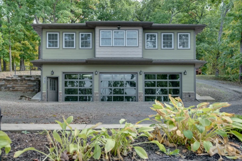 Modern two-story home with three glass garage doors surrounded by trees and landscaped grounds.