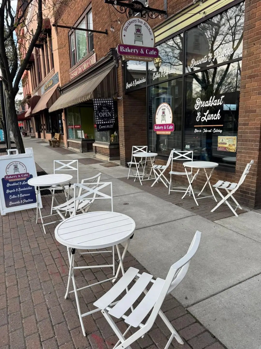Outdoor seating in front of Blackberry Inn Kitchen Bakery & Cafe with white café tables and chairs along a charming downtown sidewalk.