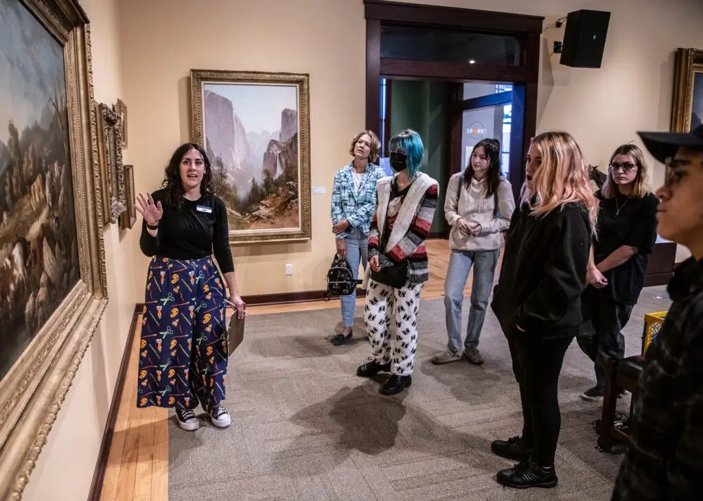 Museum guide leading a group of visitors through an art gallery while discussing landscape paintings at The Rockwell Museum.