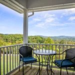 Balcony with chairs and table overlooking a scenic landscape with mountains and trees.
