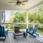 Porch with blue Adirondack chairs, a ceiling fan, and a view of greenery.