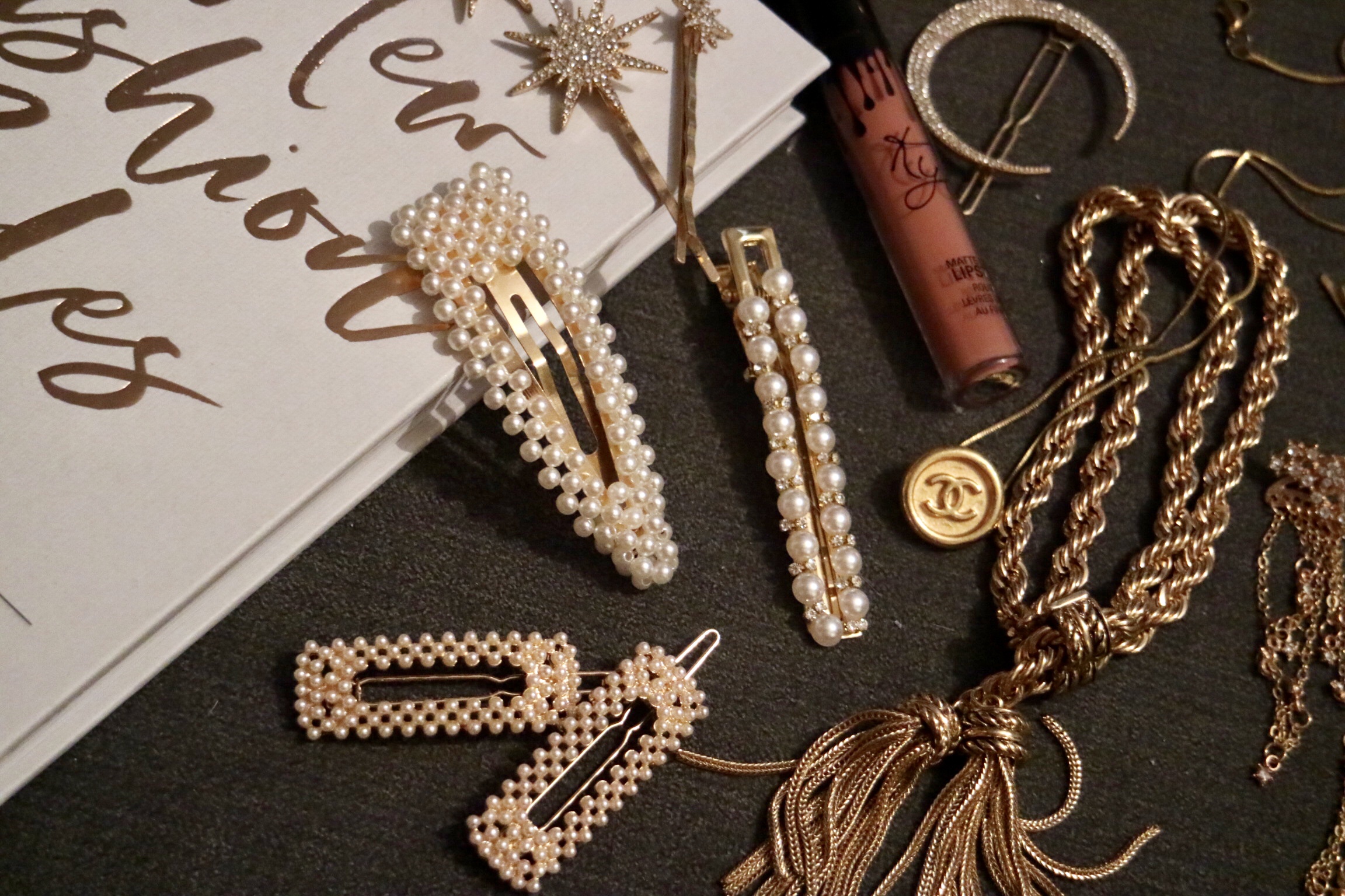 A selection of pearl hair clips, a Chanel necklace and tassel bracelet draped across a grey back ground and book