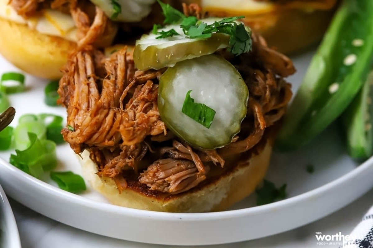 Mouthwatering pulled pork sliders topped with tangy pickles, served on a plate.