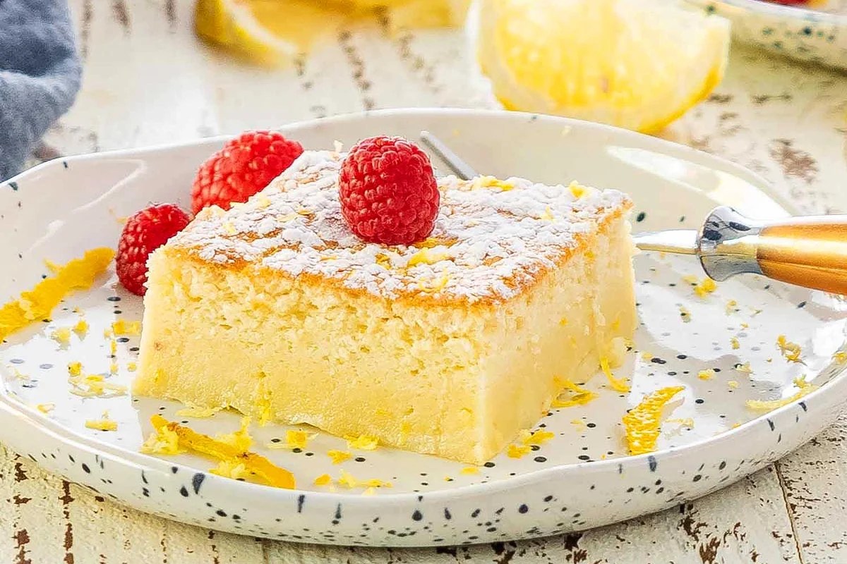 A slice of lemon cake garnished with raspberries and dusted with powdered sugar, presented on a decorative plate, perfect for church potluck desserts.