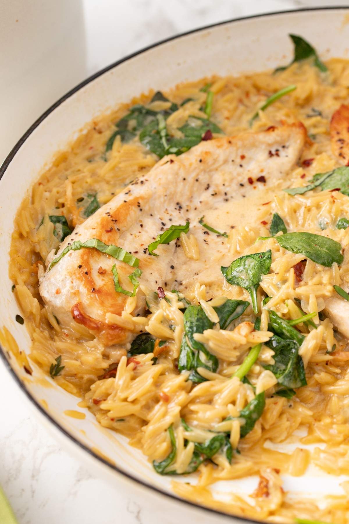 A skillet containing creamy Tuscan chicken breasts, spinach, and creamy orzo pasta.